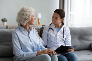 Caring young woman nurse helping supporting old adult grandmother patient