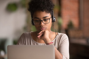 Focused african american girl student wearing headphones looking at laptop